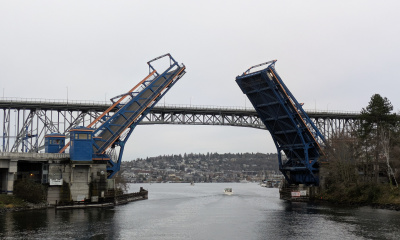 Drawbridge raised over a river with a distant cityscape background.